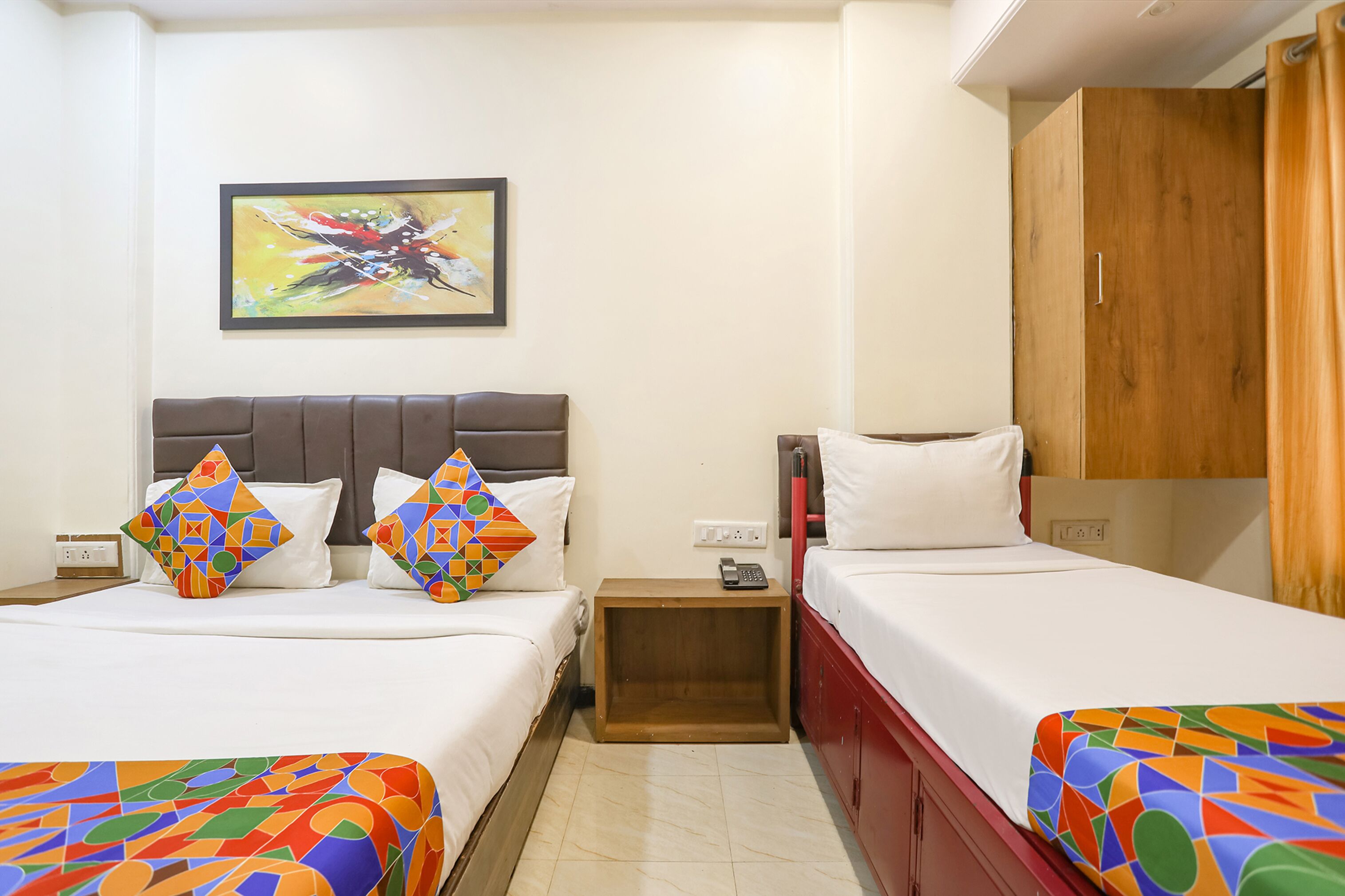 Quarto de hotel com duas camas, um guarda-roupa de madeira, uma mesa de cabeceira pequena e um quadro na parede.