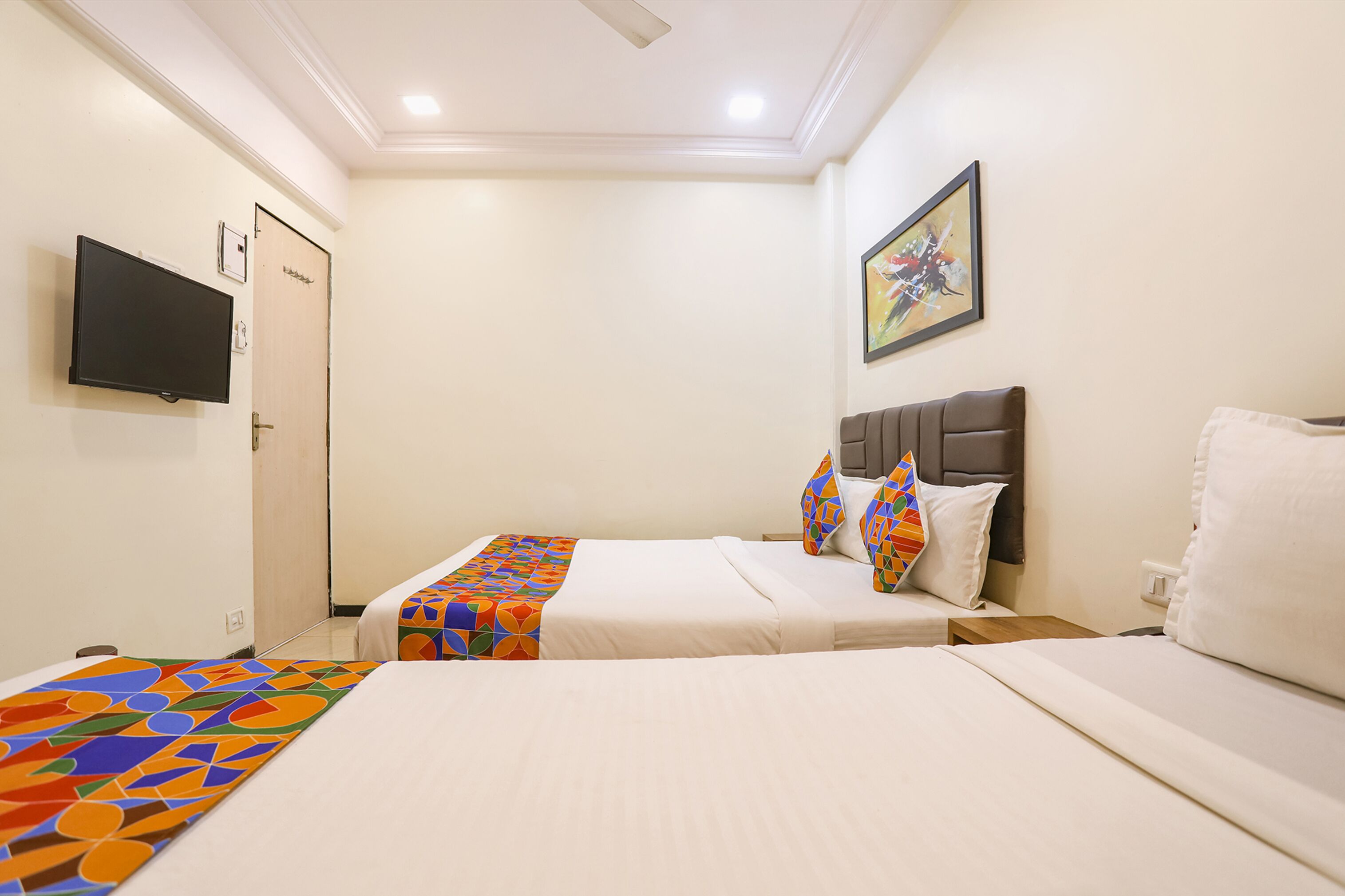 A hotel room with two beds, a television on the wall, and a painting above the headboard.