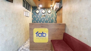 A reception area with a wooden desk, a red couch, and three wall clocks. - FabHotel Aksa Inn (Mumbai)
