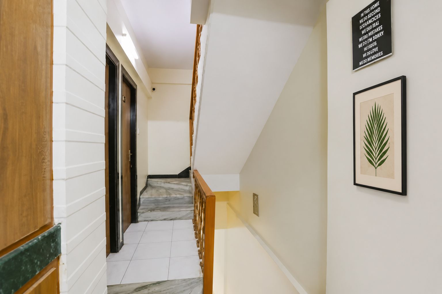 A hallway with a marble staircase, wooden doors, and a framed leaf artwork on the wall.