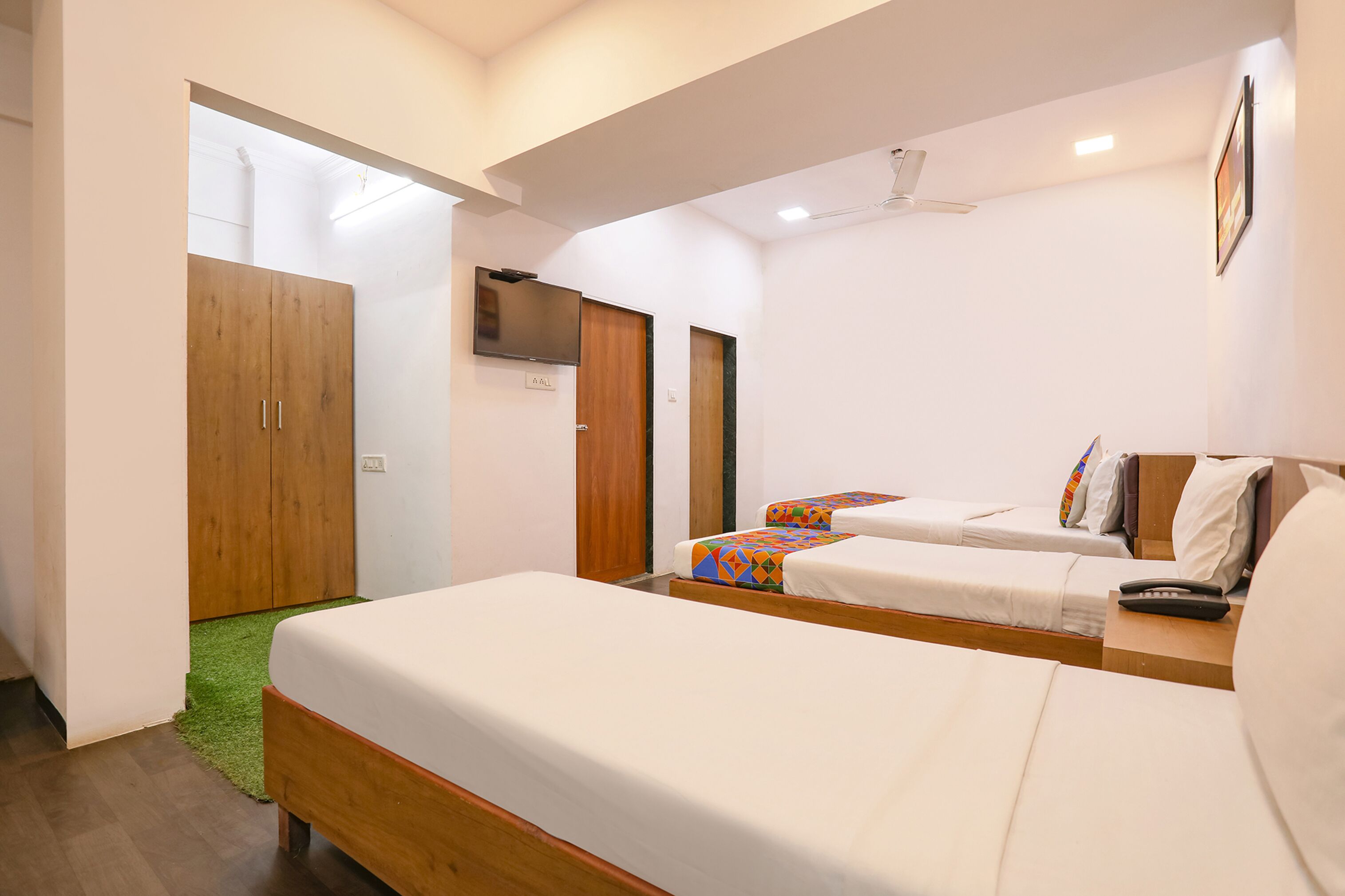 A hotel room with two beds, a wooden wardrobe, a television, and a green carpet.