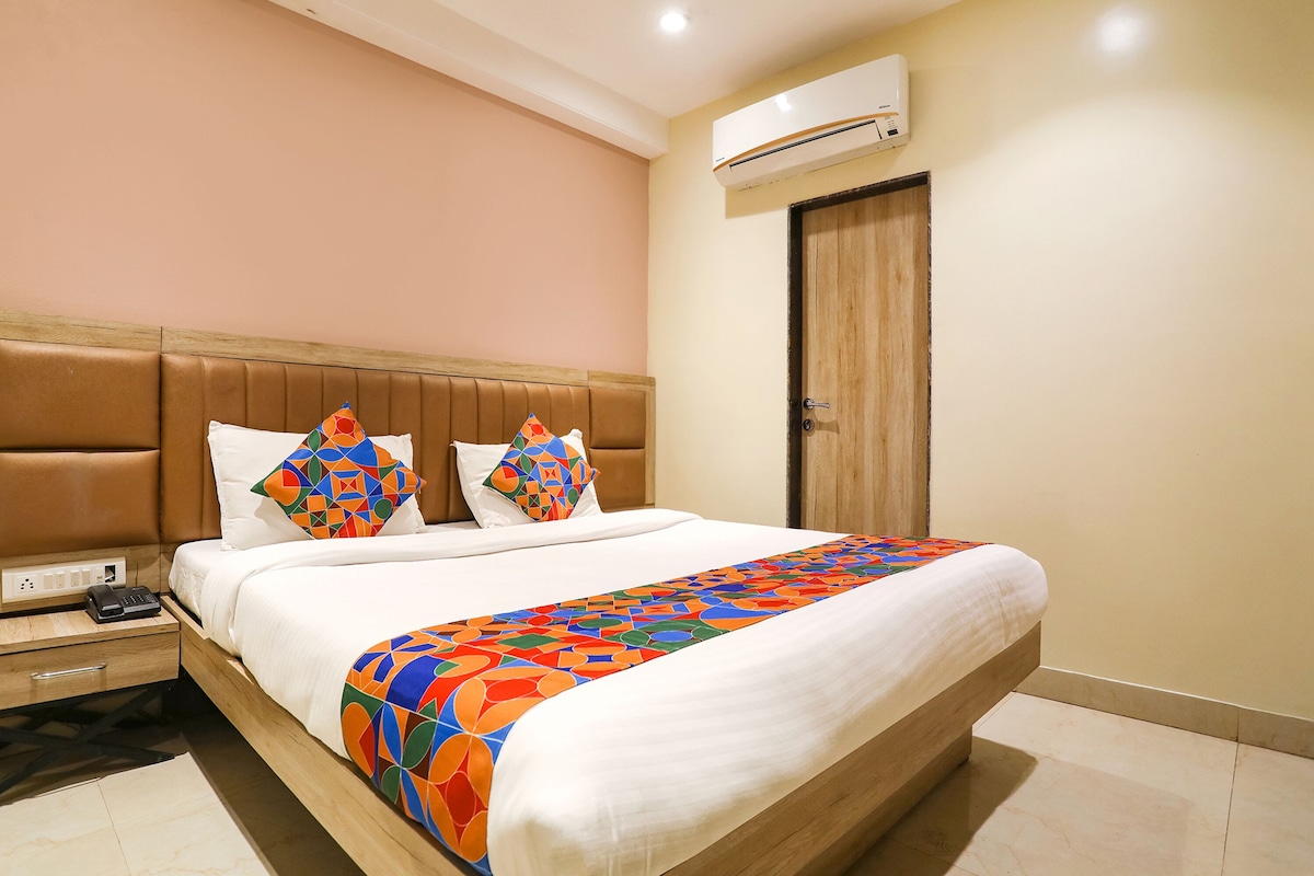 A hotel room with a large bed, a wooden headboard, a bedside table with a phone, and an air conditioning unit on the wall.