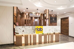 Hotellin vastaanottotiski, jossa on «Fab Hotels» -kyltti, puupanelointi ja marmorinen palvelutiski.