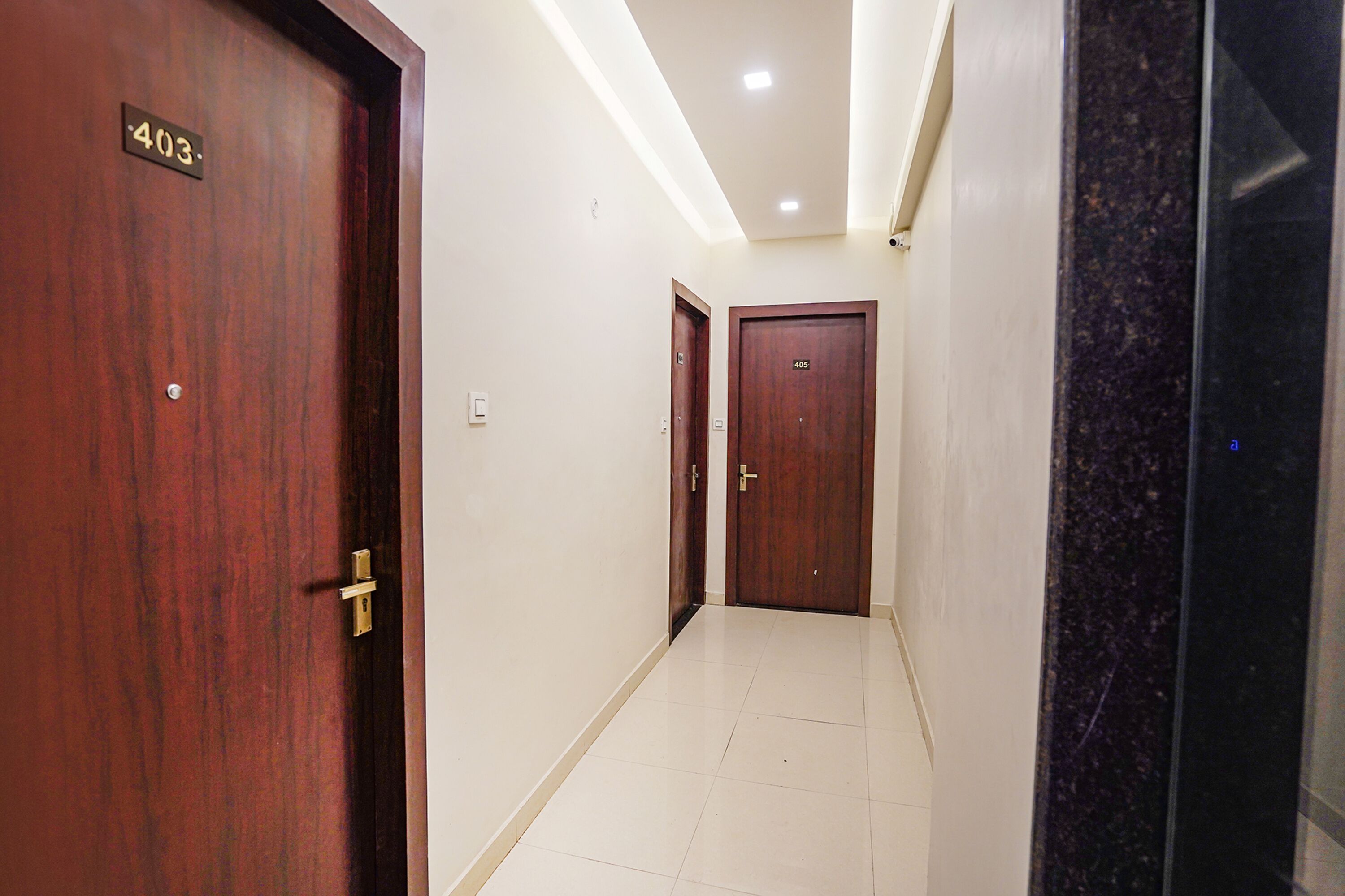 A hallway with wooden doors numbered 403 and 405, white tiled flooring, and recessed ceiling lighting.