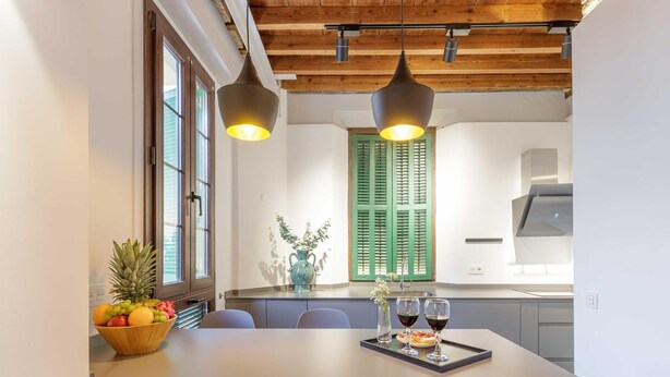 Une cuisine moderne dotée d’un îlot central, de poutres en bois au plafond et d’un coin repas avec une table dressée pour deux personnes.