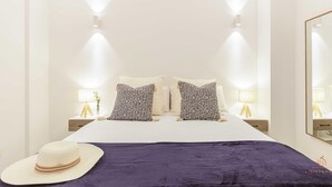 Une chambre à coucher avec un lit, deux tables de chevet, un miroir et un chapeau posé sur le sol.