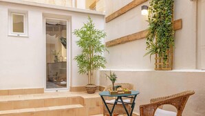 Un petit espace patio agrémenté d’un bambou en pot, de meubles en osier et d’un sol carrelé.