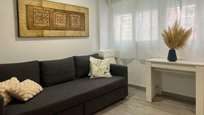 A modern living room with a dark grey sofa, a white radiator, a large decorative wall piece, and a window with sheer curtains.