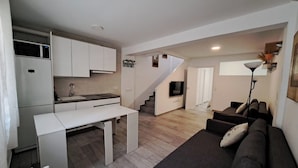 A compact living space with a kitchenette, a dining area, a sofa, and a staircase leading to another room.