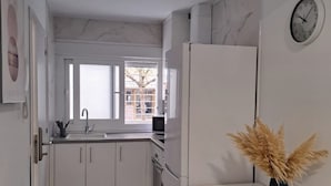 A modern kitchen with white cabinets, a white refrigerator, a dining table with a chair, and a clock on the wall.