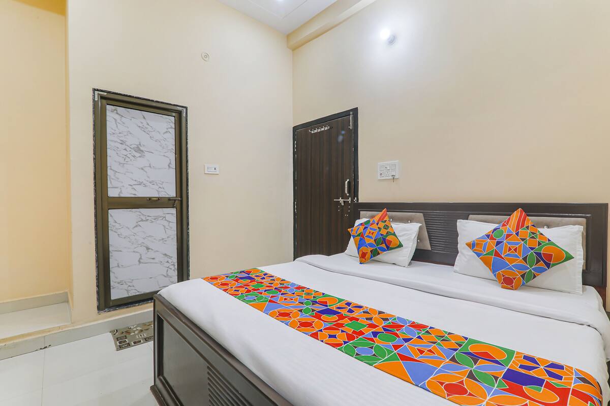 A neatly made bed with a colorful geometric bedspread, a marble-framed window, and a dark wooden door.