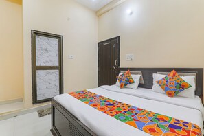 A neatly made bed with a colorful geometric bedspread, a marble-framed window, and a dark wooden door. - Fabexpress Saryu (Faizabad)