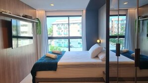 Ein modernes Hotelzimmer mit einem großen Bett, einem Schreibtisch mit Stuhl und einem großen Fenster mit Blick auf die Stadt.