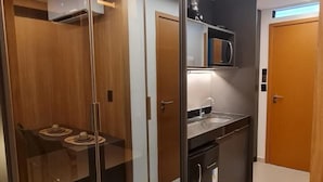 Eine moderne Küche mit integriertem Mikrowellenherd, einer Kaffeemaschine und einem Spülbecken. Durch eine Glastrennwand ist ein Holzessttisch mit Stühlen zu sehen.