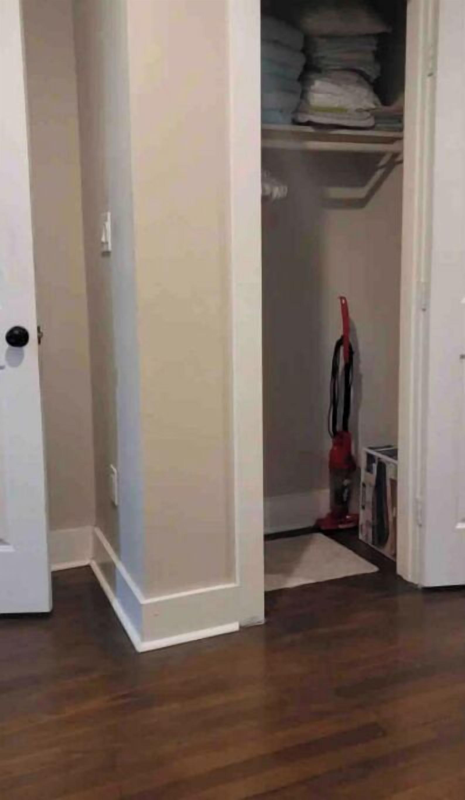 A hallway with a closet containing folded clothes and a vacuum cleaner.
