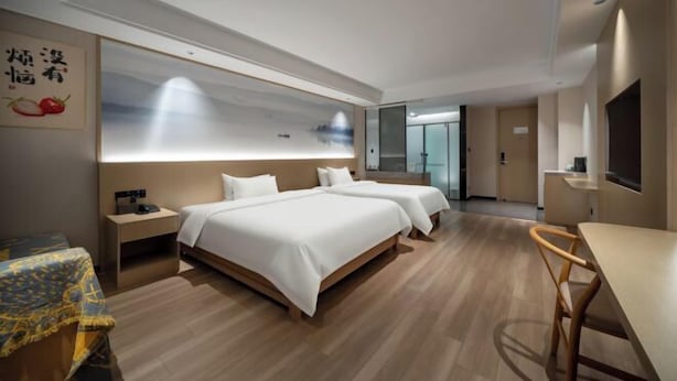 A hotel room with two beds, a desk, a chair, a TV, and a large window. - Manju Hotel (Shaoxing)