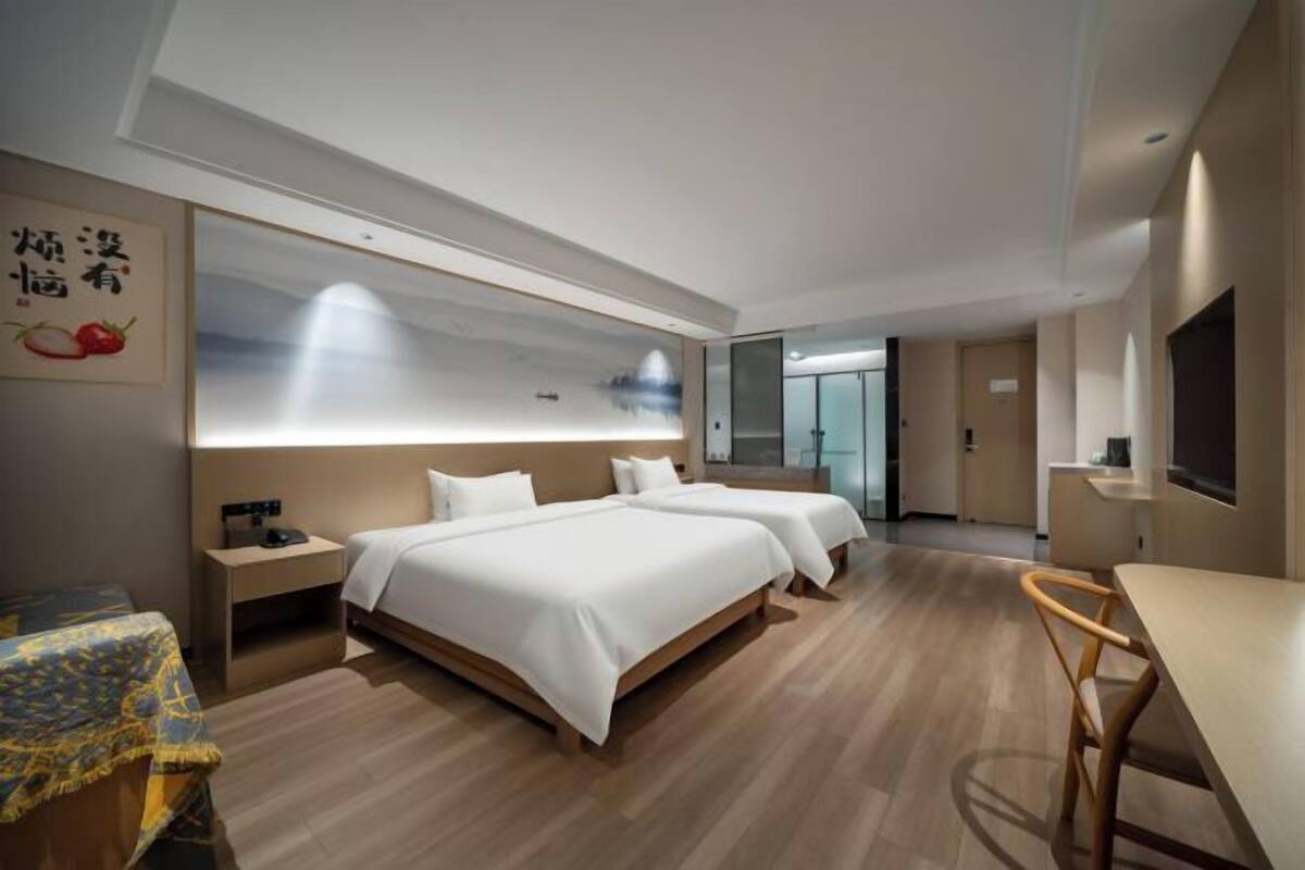 A hotel room with two beds, a desk, a chair, a TV, and a large window.