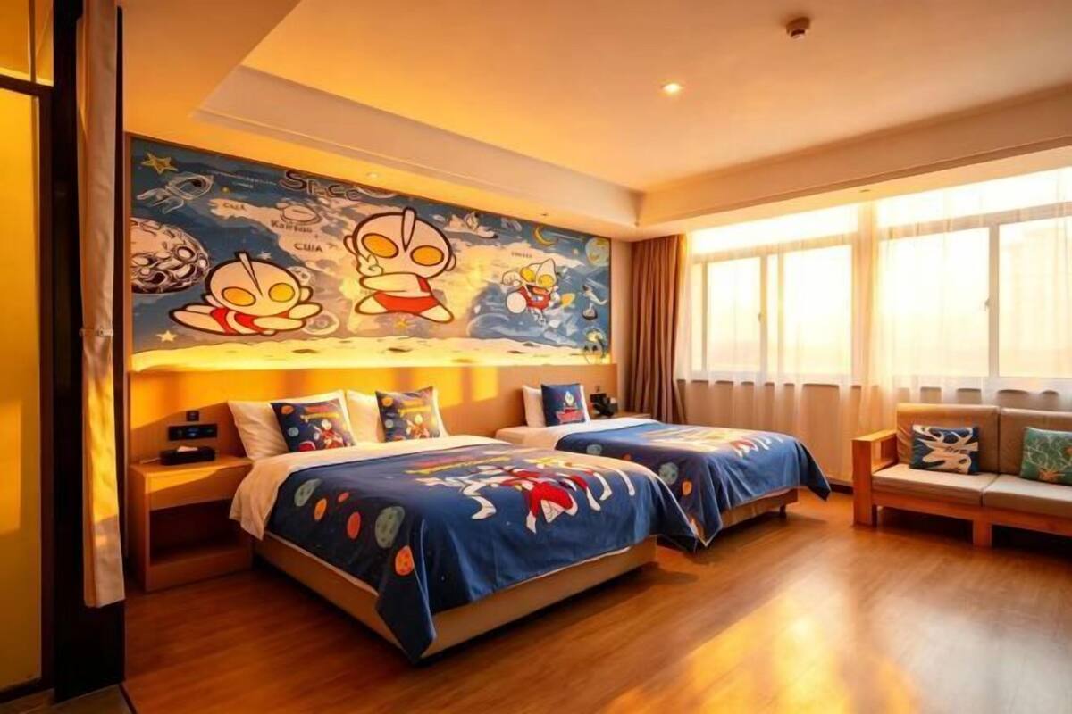 A hotel room with two beds, a mural on the wall, a window with curtains, and a wooden floor.