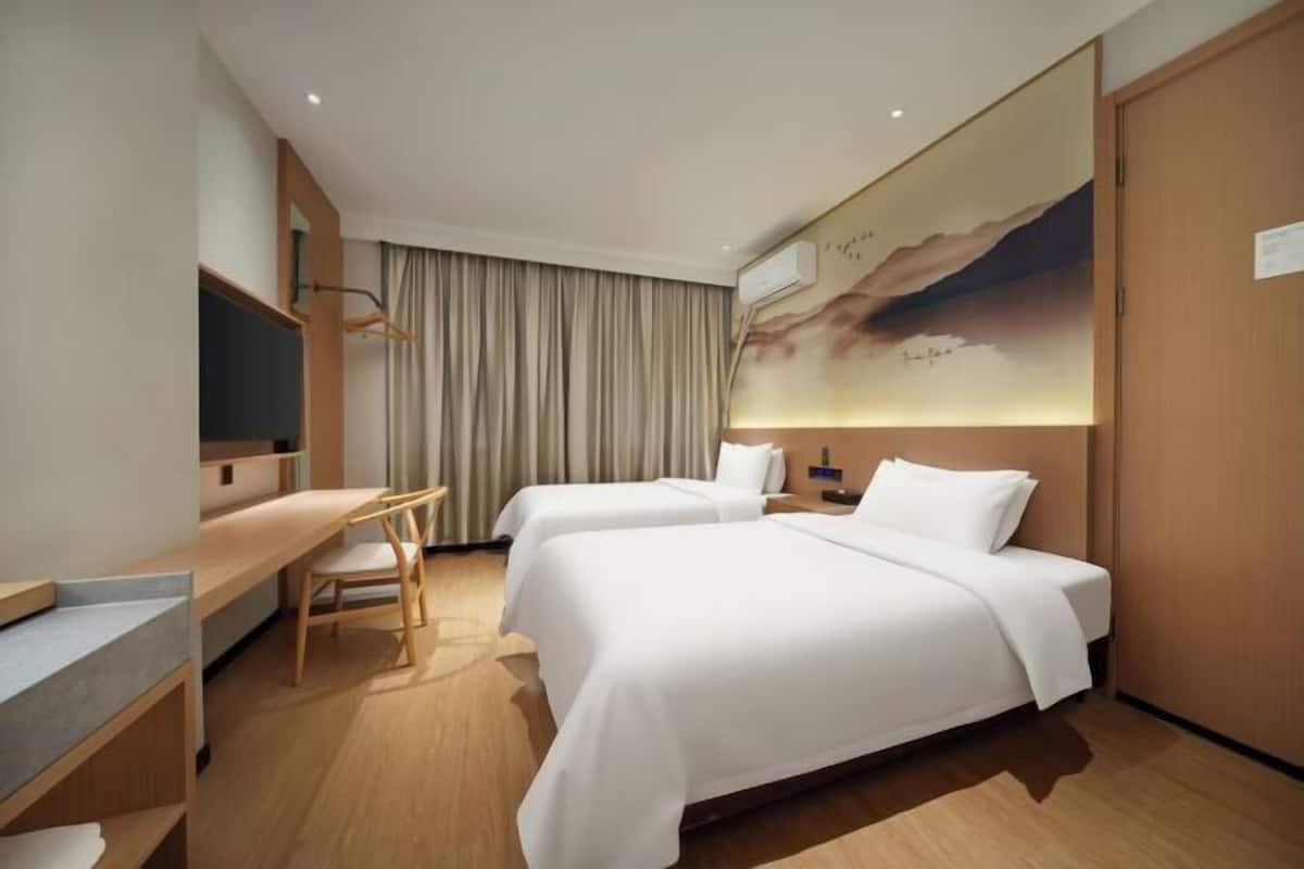 A hotel room with two beds, a desk, a chair, a TV, and a painting on the wall.