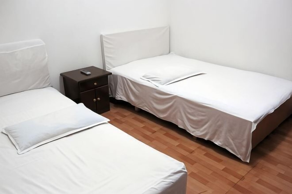 A room with two single beds, a small bedside table, and a wooden floor.