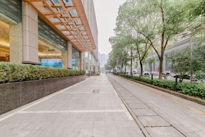 A wide, clean sidewalk with a modern building on one side and a row of trees on the other. - Hubei East Lake Hotel (Wuhan)