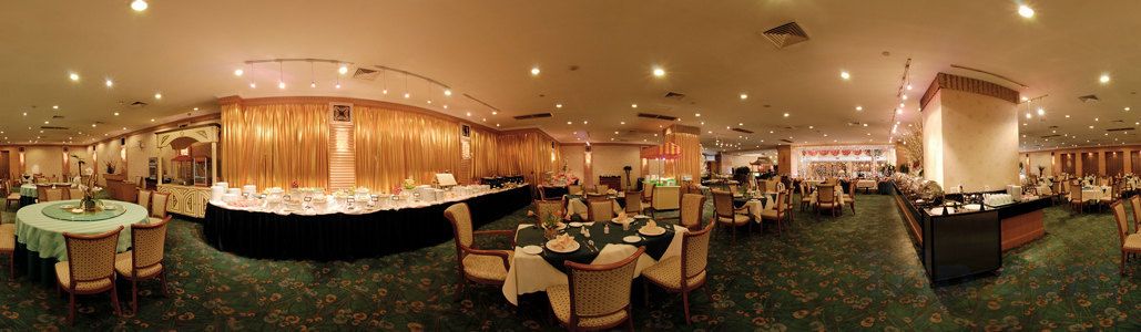 Un salón de banquetes con mesas redondas, una zona de buffet y un mostrador de recepción.