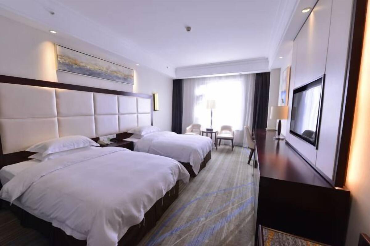 Een hotelkamer met twee bedden, een bureau, een televisie en een raam met gordijnen.