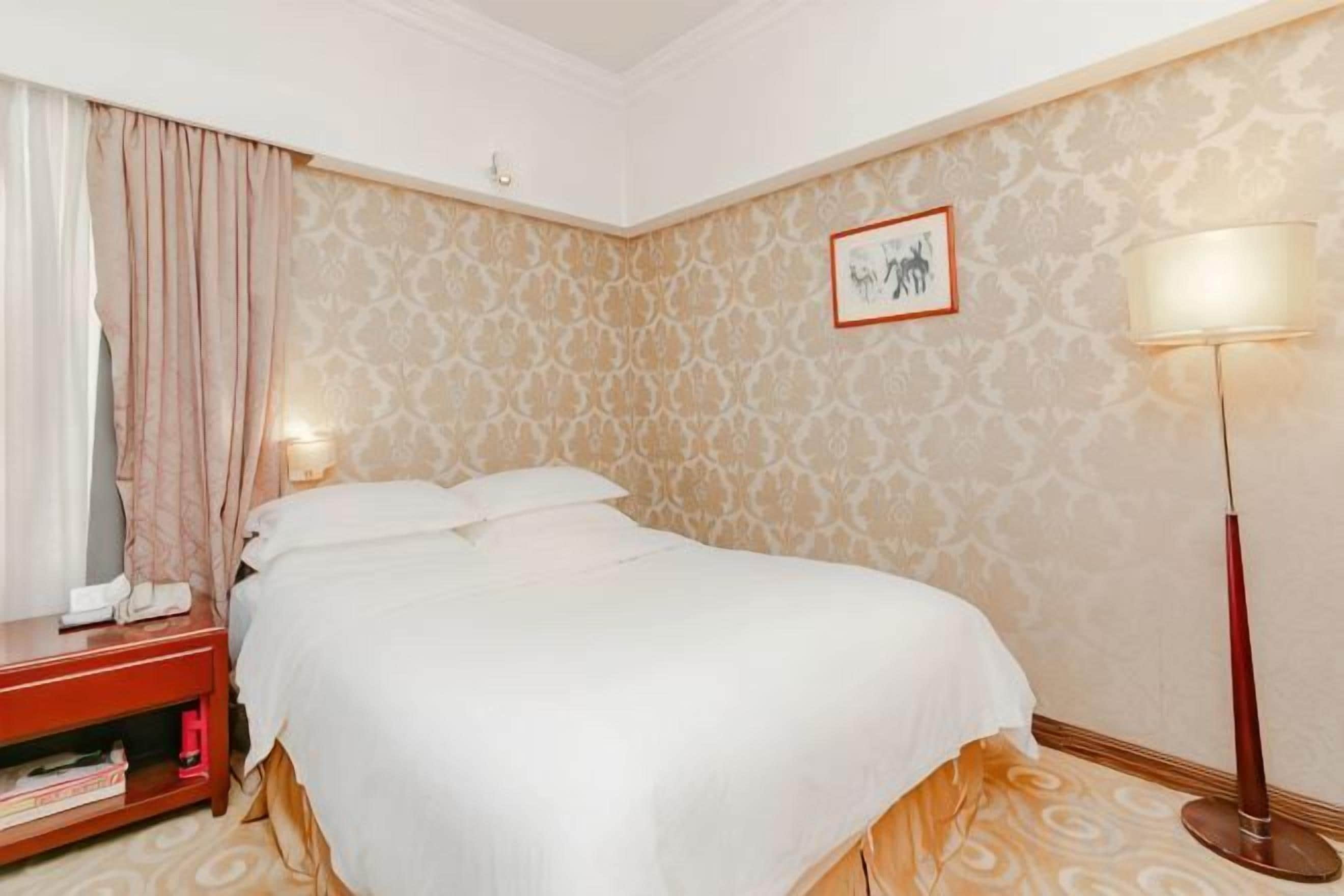 Une chambre d’hôtel avec un lit, une table de chevet, une lampe et un mur décoré d’un motif.