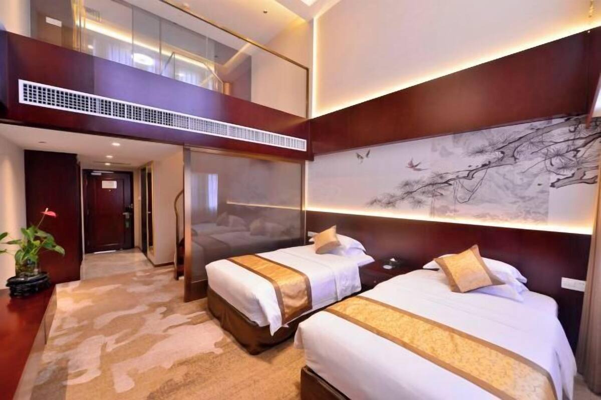 Een hotelkamer met twee bedden, een groot raam, een decoratieve muur en een trap.