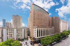 A multi-story hotel with a prominent corner entrance, large windows, and a parking area with cars.
