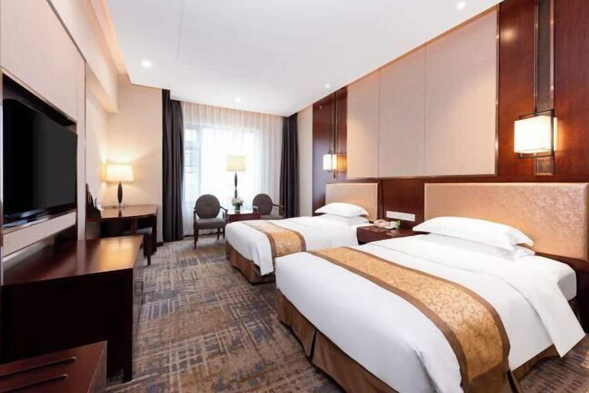 Een hotelkamer met twee bedden, een televisie, een bureau en een stoel.