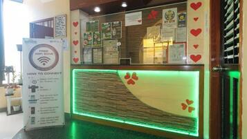 A reception desk with a glass partition, a digital display, and a sign with Wi-Fi information.