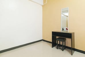 Ein Zimmer mit weißer Wand, einer beigen Wand, einem Spiegel mit schwarzem Rahmen, einem Schreibtisch mit schwarzem Rahmen und einem schwarzen Hocker.