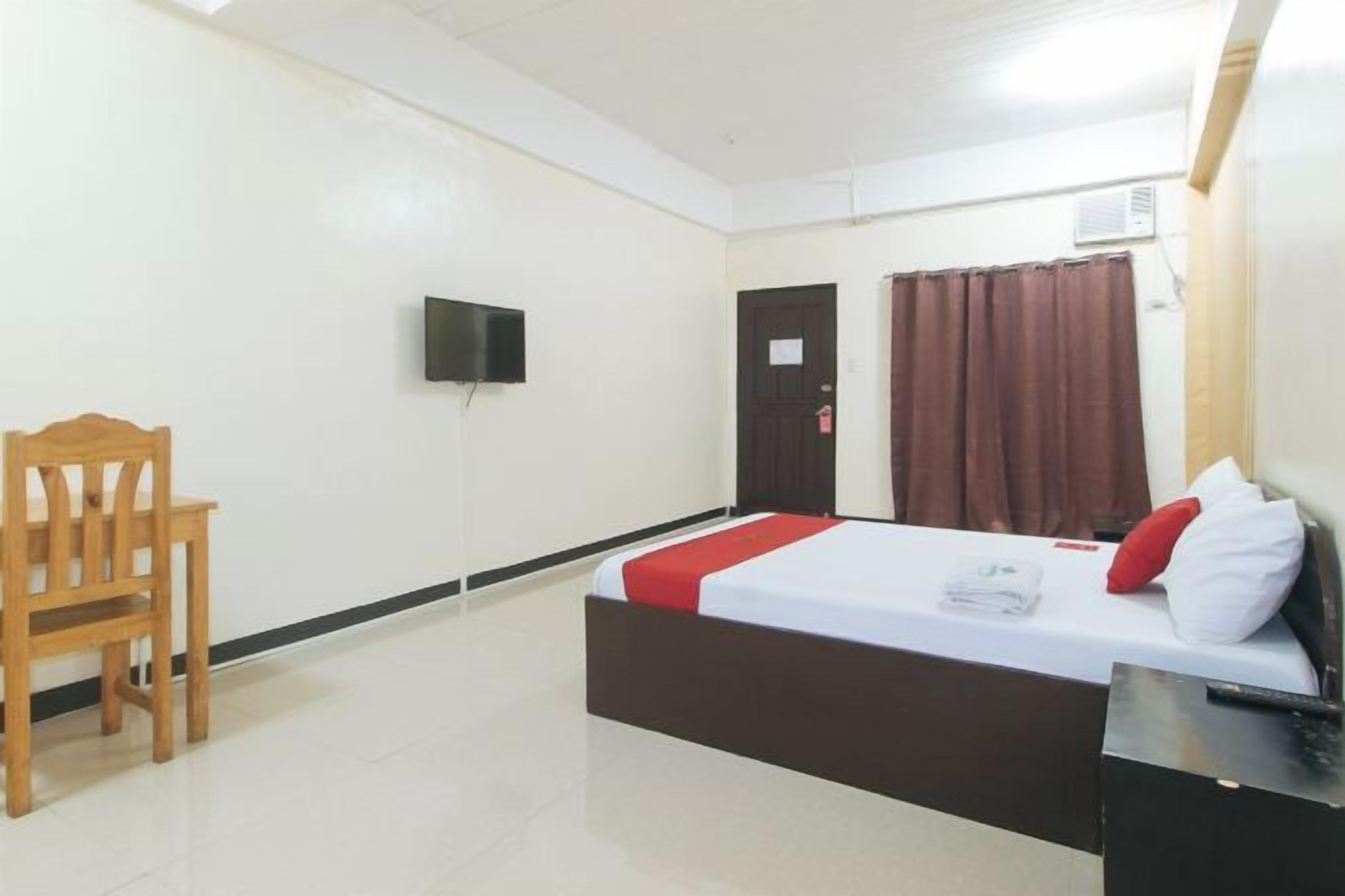 Een hotelkamer met een bed, een houten stoel, een televisie, een deur en een raam met gordijnen.