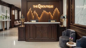 Una recepción con el rótulo 'The Boutique', dos áreas de recepción identificadas como 'Recepción' y 'Oficina de excursiones', y una zona de estar con una mesa redonda y dos sillas.