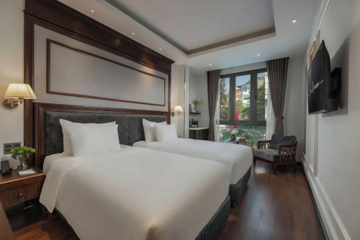 A hotel room with two beds, a TV mounted on the wall, a balcony with a view, and a small seating area.