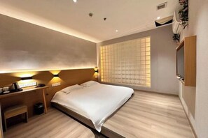 Una habitación de hotel con cama, mesita de noche, lámpara y ventana con persianas.
