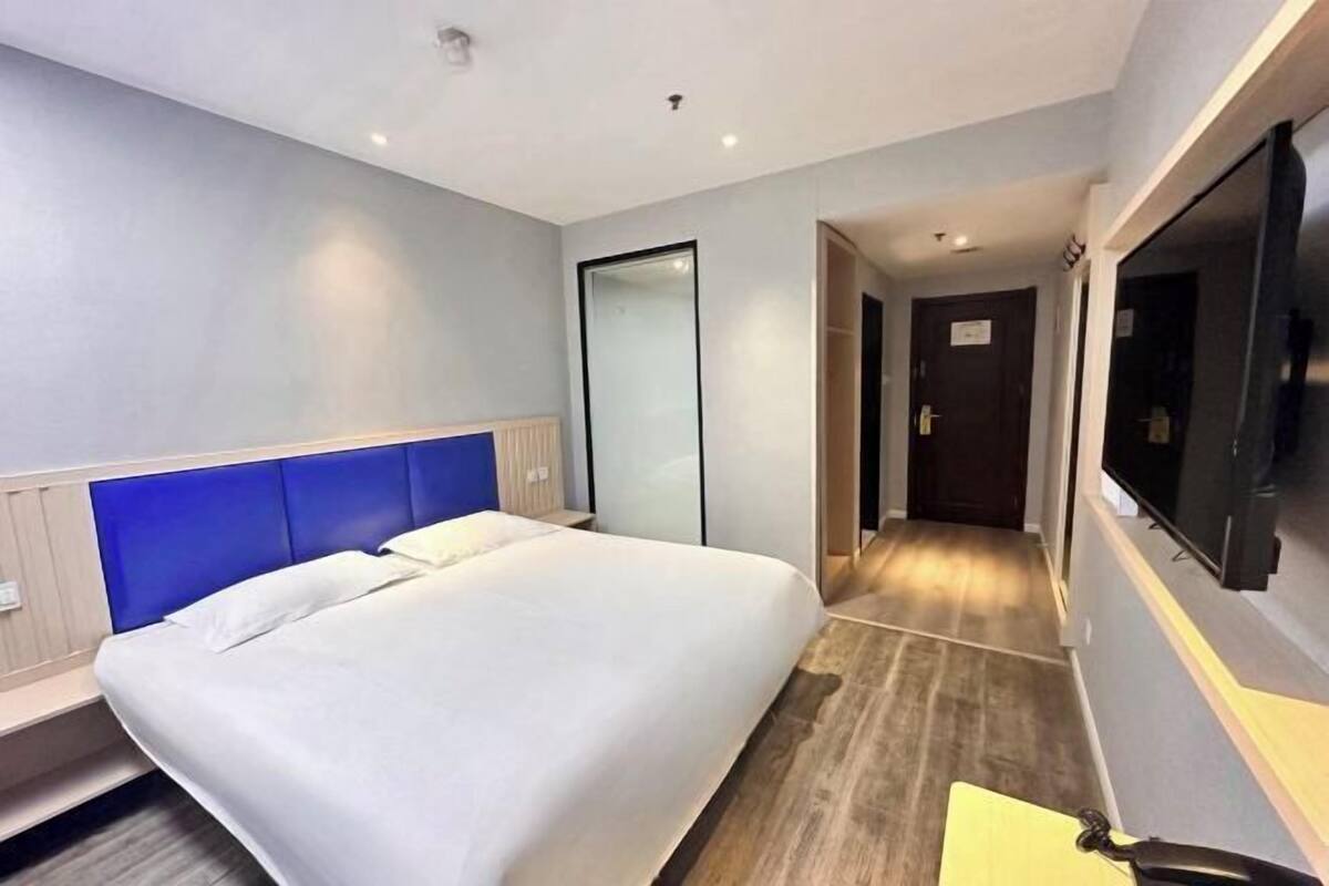 A hotel room with a bed, a television, a mirror, and a wooden floor.