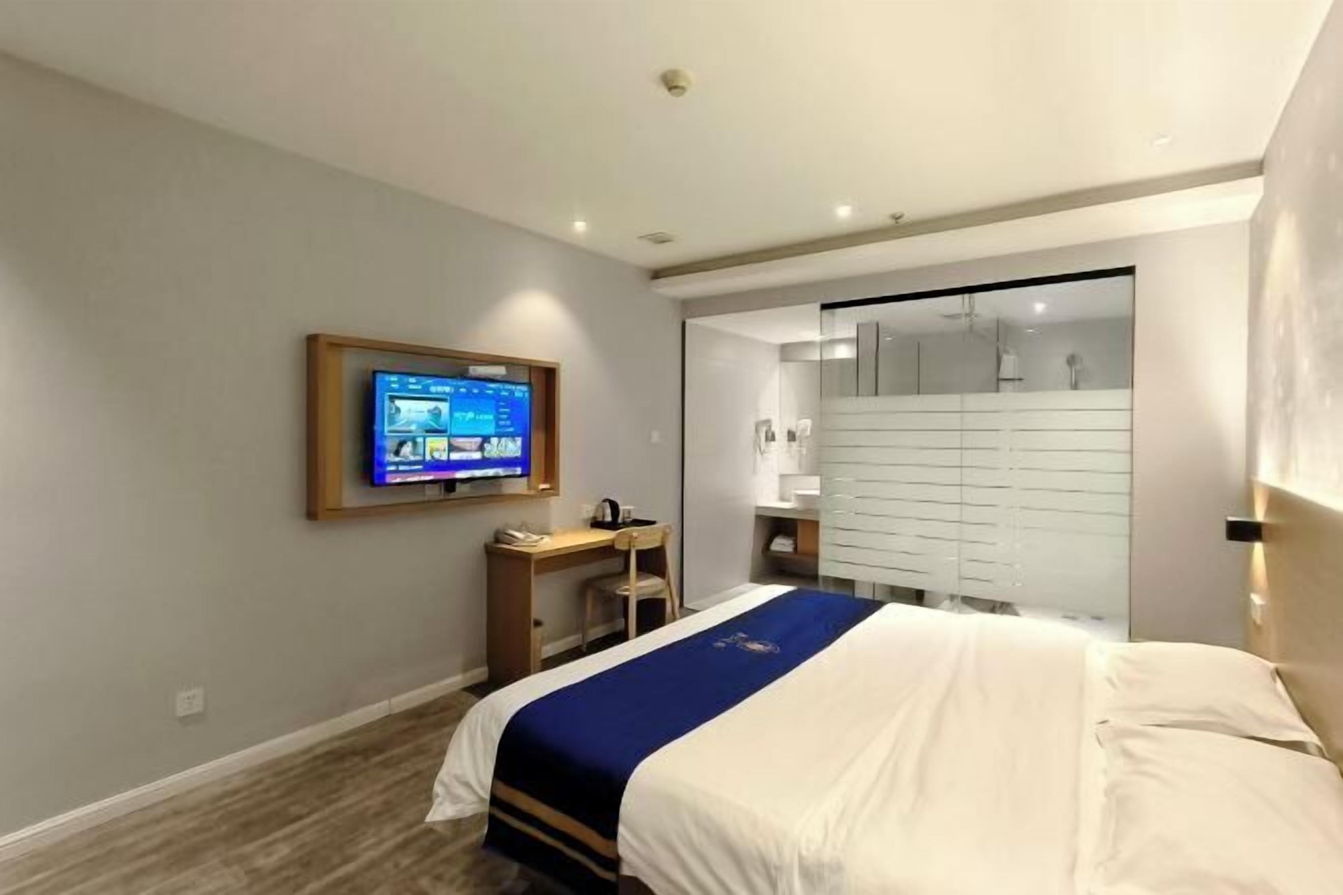 Quarto de hotel com cama, escrivaninha, televisão e guarda-roupa.