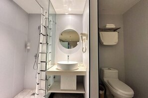 Un baño moderno con cabina de ducha de vidrio, un espejo redondo, un lavamanos blanco y un inodoro.
