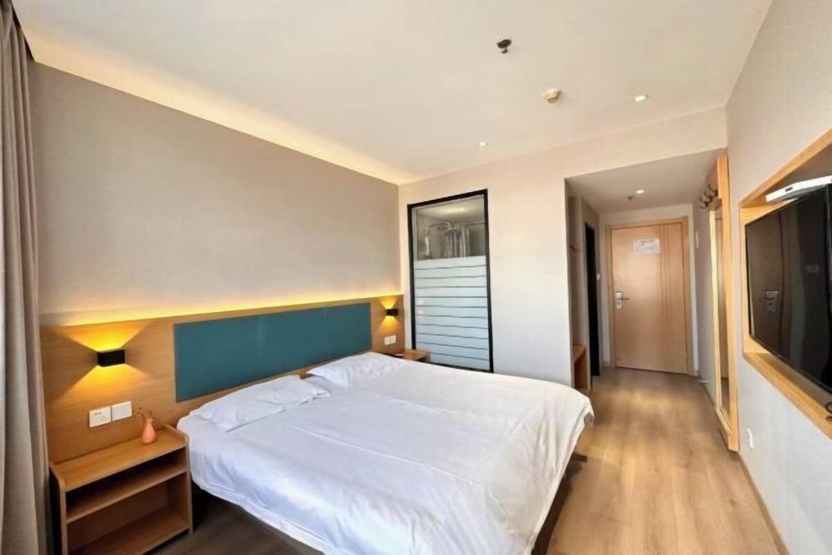 A hotel room with a bed, bedside tables, a wall-mounted light, and a door leading to another room.