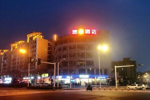 Un immeuble à plusieurs étages, doté d’une enseigne lumineuse, de lampadaires et d’un passage piéton.