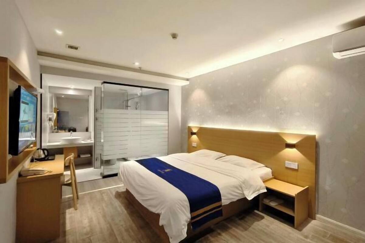 A hotel room with a bed, bedside tables, a desk, a chair, a television, and a bathroom with a shower and toilet.