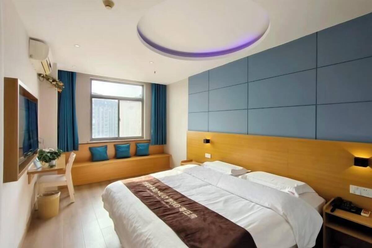 A hotel room with a bed, a desk with a chair, a window with curtains, and a wall-mounted TV.