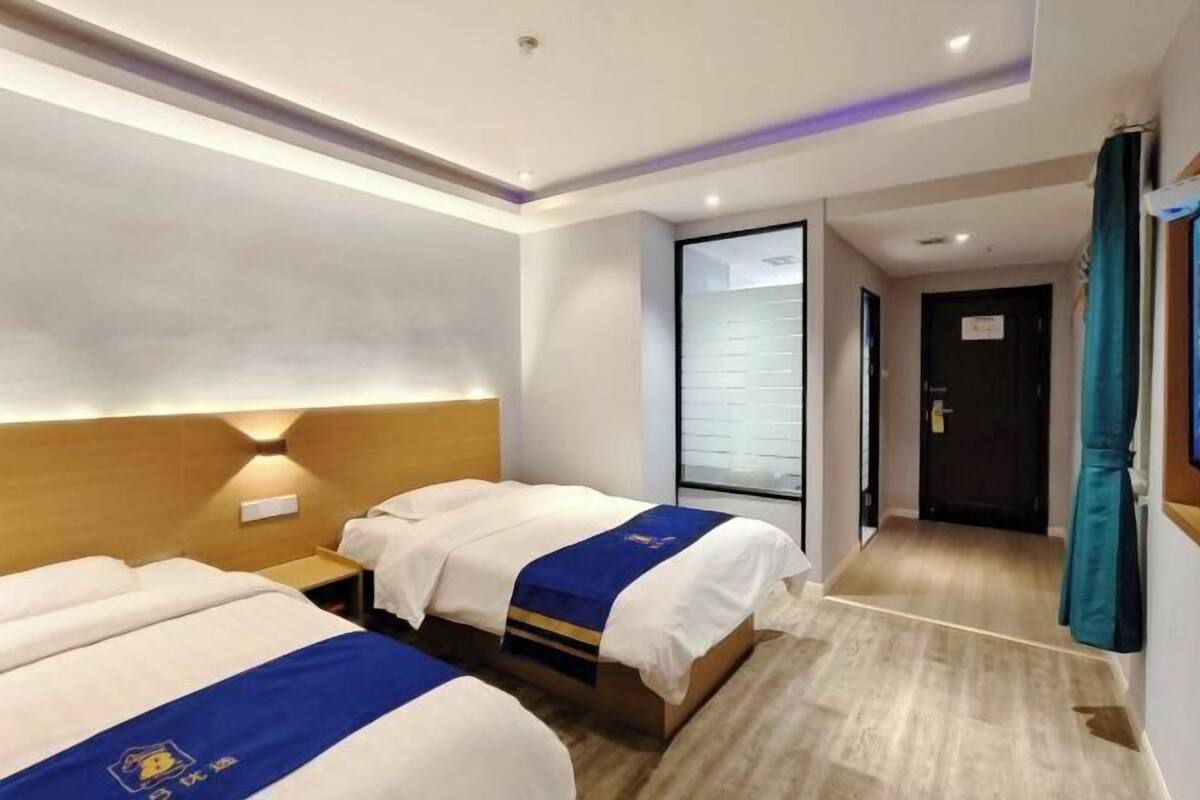 A hotel room with two beds, a wooden headboard, a nightstand, and a view of the hallway.