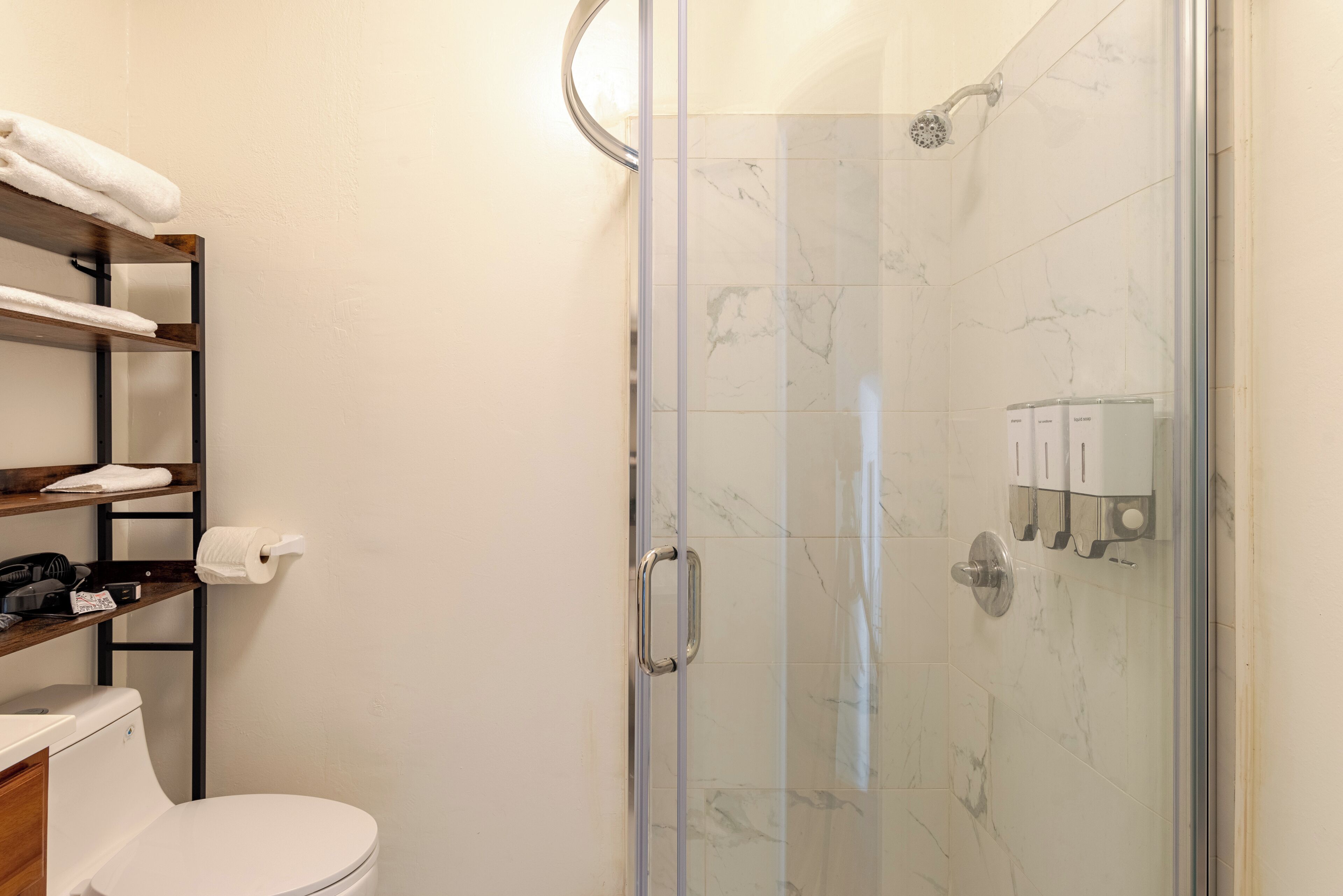 Un bagno moderno con doccia vetro, piastrelle in marmo, un water e mensole con asciugamani e articoli da toilette.