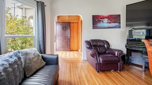 Un soggiorno con pavimento in legno, un divano in pelle, una poltrona scura, un pianoforte e un quadro appeso al muro.