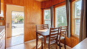 Una stanza con rivestimenti in legno, un tavolo da pranzo e sedie, ampie finestre con tende e vista sull'esterno.