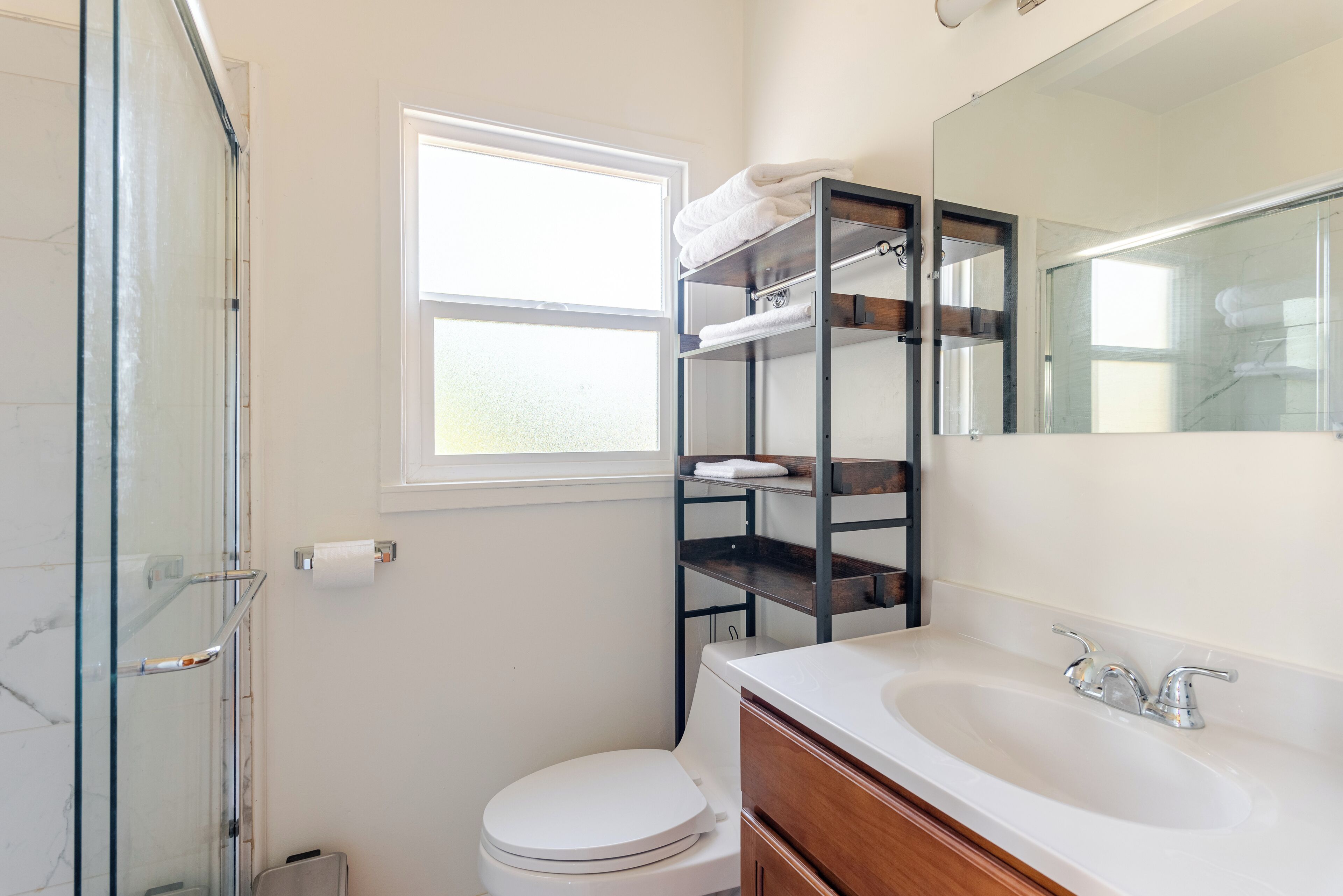 A bathroom with a glass shower enclosure, a white toilet, a vanity with a sink, and a mirror.