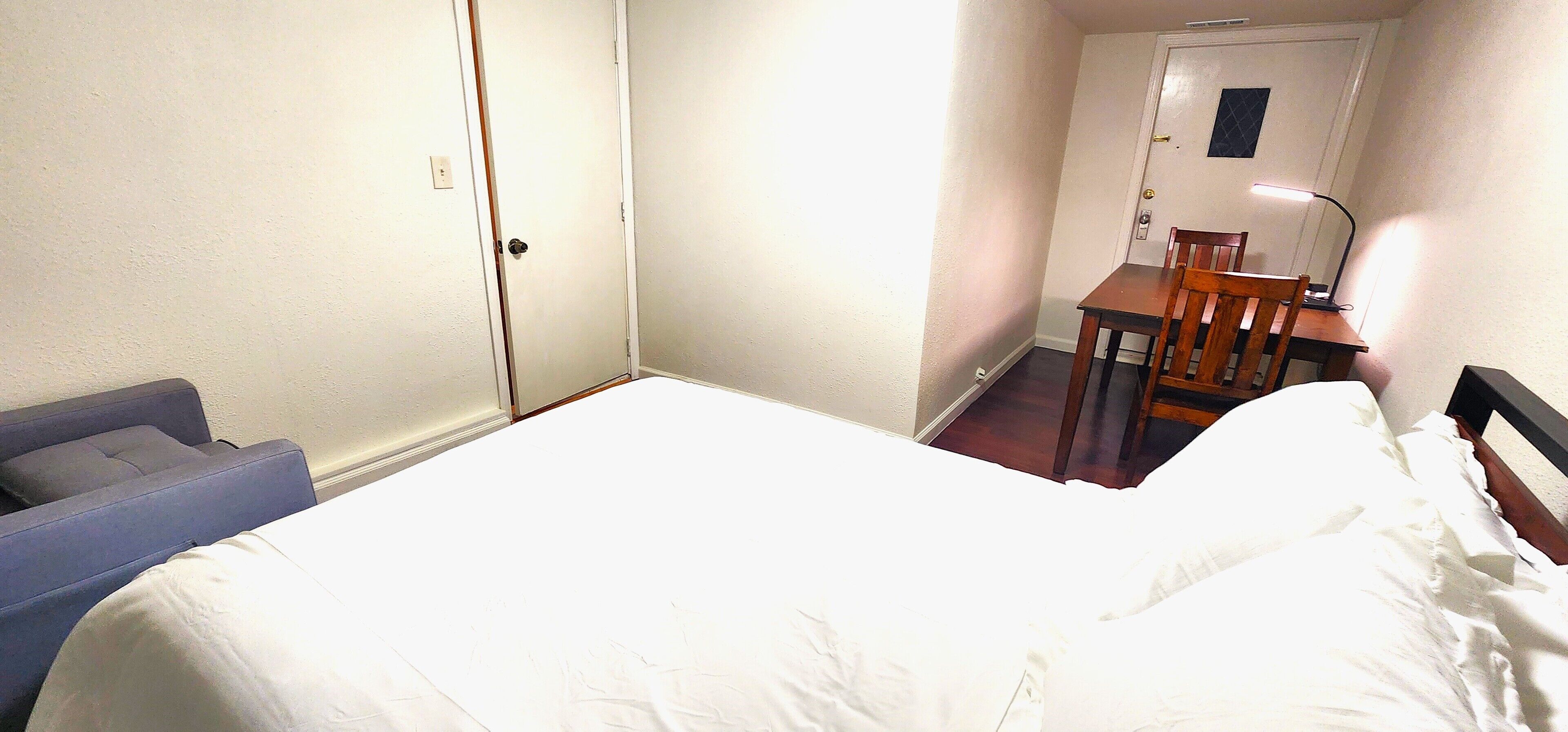 A hotel room with a bed, a desk with a chair, and a door.